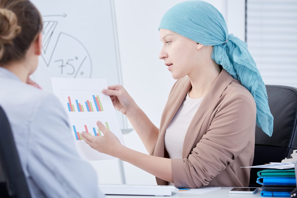 A woman with cancer and covered head discussing charts with her doctor.